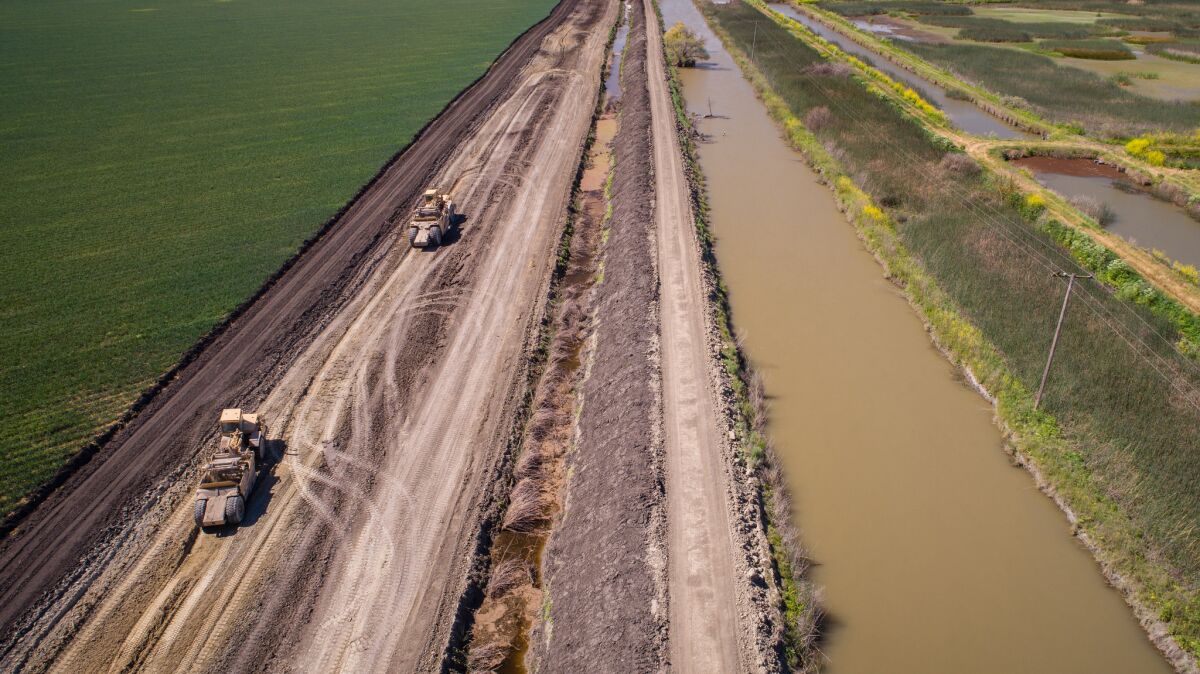Earth movers carry dirt from a farm field to shore up levees at the Kings River and Fresno Slough in preparation for coming snowmelt. (Tomas Ovalle / For The Times)