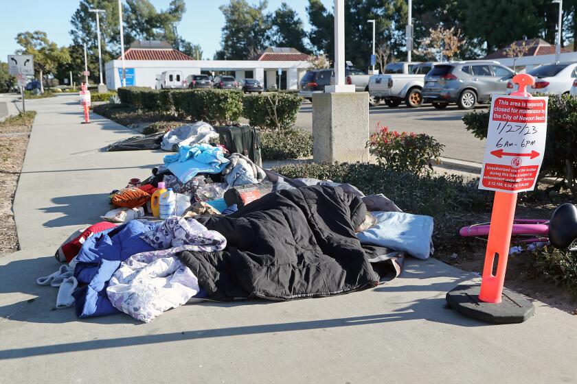 A woman sleeps along the sidewalk in front of the Newport Transportation Center on Thursday morning in Newport Beach. A group of homeless people said they are being treated unfairly by both the city and the OCTA. (Kevin Chang / Daily Pilot)