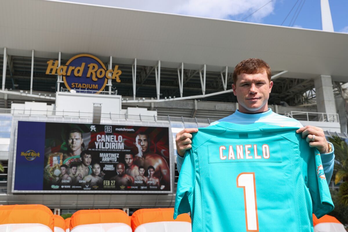 Canelo Alvarez holds up a personalized Miami Dolphins jersey while at Hard Rock Stadium.