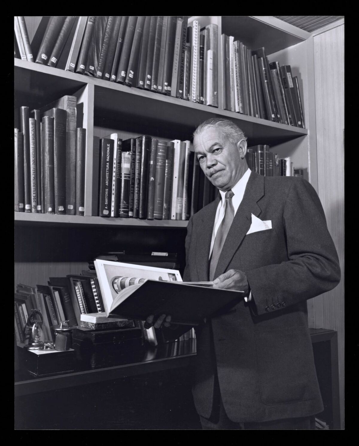 A black-and-white portrait shows architect Paul Williams standing in a library holding a book.