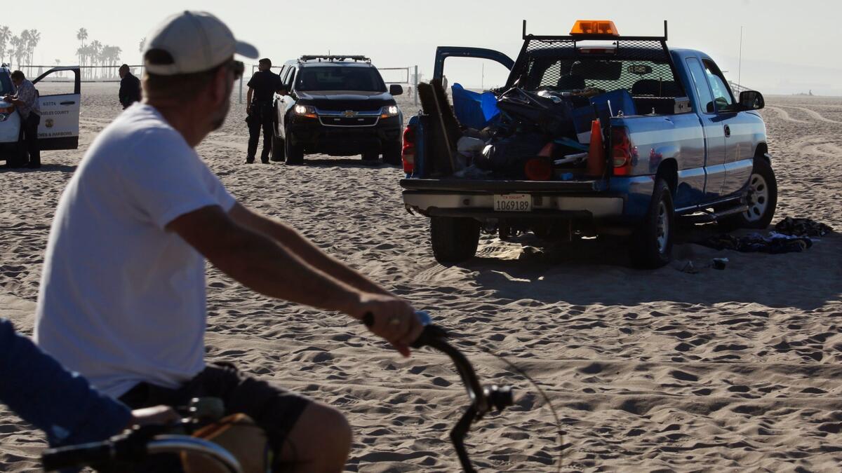 A bicyclist looks over a scene, right, where a 53-year-old man suffered serious injuries when a Los Angeles County Beaches and Harbor vehicle ran over him in Venice Beach Friday morning.