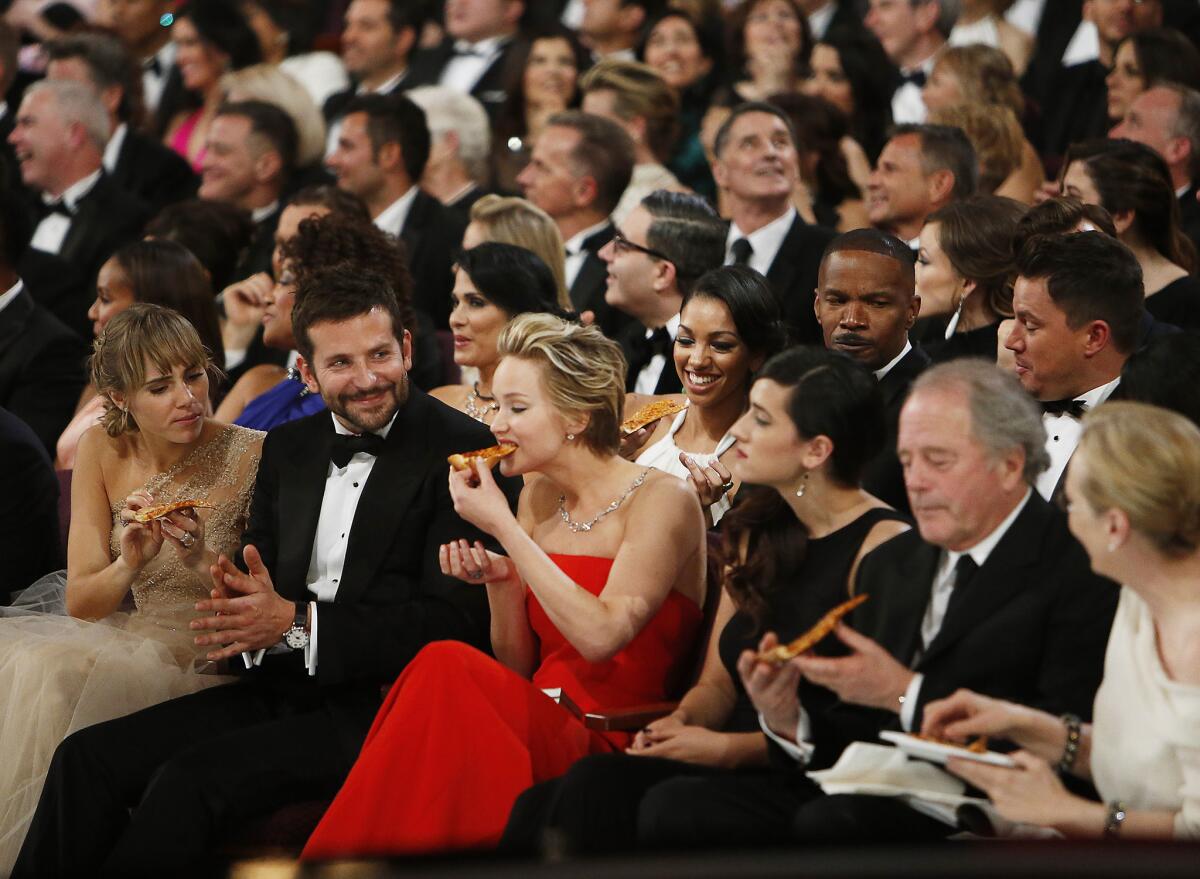 Ellen DeGeneres hands out a pizza she ordered from backstage as Jennifer Lawrence eats and Bradley Cooper looks on at the 86th Annual Academy Awards on March 2, 2014 at the Dolby Theatre at Hollywood & Highland Center in Hollywood.