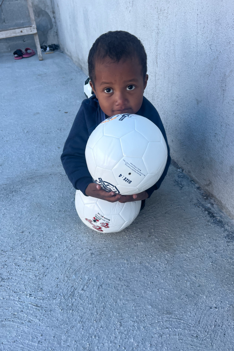 墨西哥雷诺索的 Senda de Vida 移民庇护所里，一名小男孩拿着两个足球。