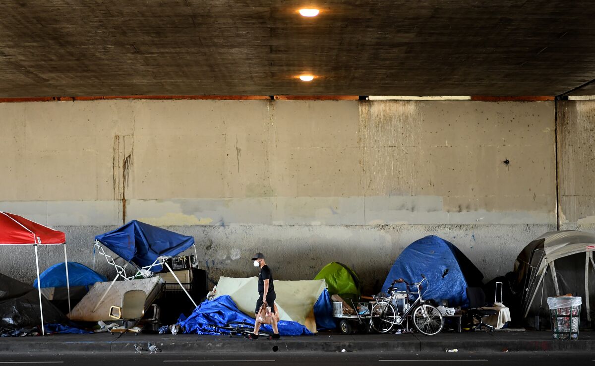 A man walks by a homeless encampment on Venice Boulevard under the 405 Freeway. A federal judge has ordered the city and county of Los Angeles to relocate thousands of homeless people living near freeways starting on Friday. 