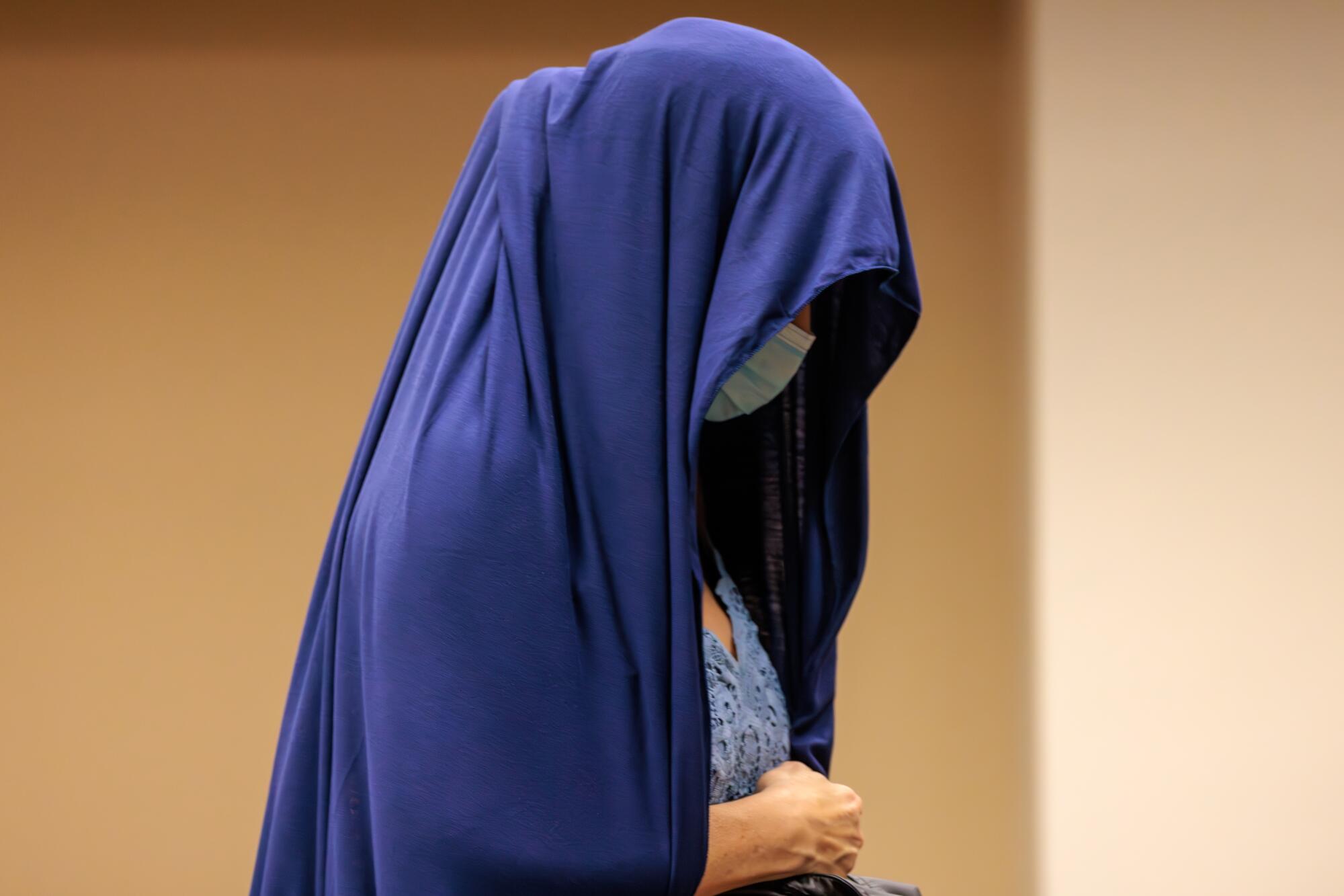 Monique Matthews covers her head with a blue sheet and face mask in court