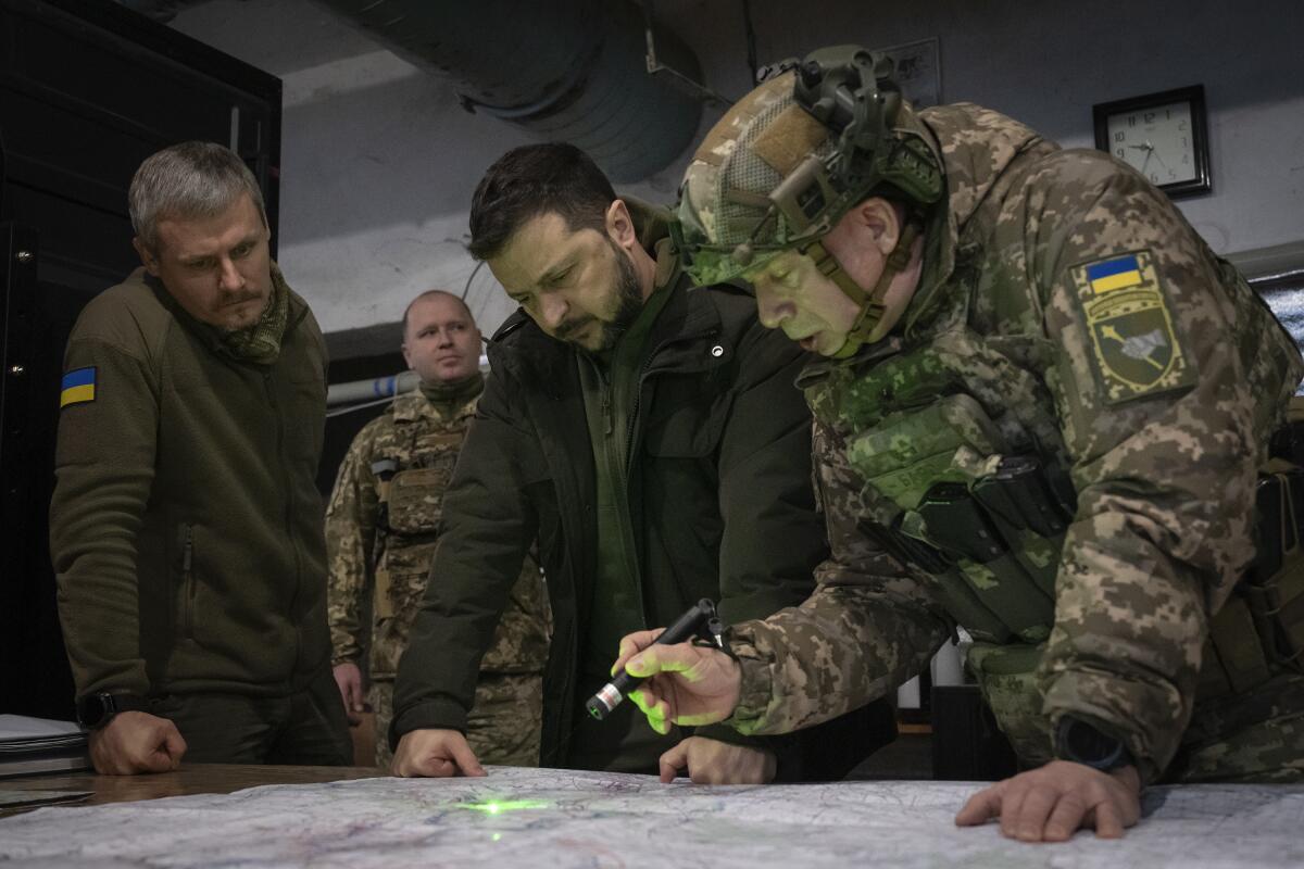 Volodymyr Zelensky looks at a map with military and government officials 