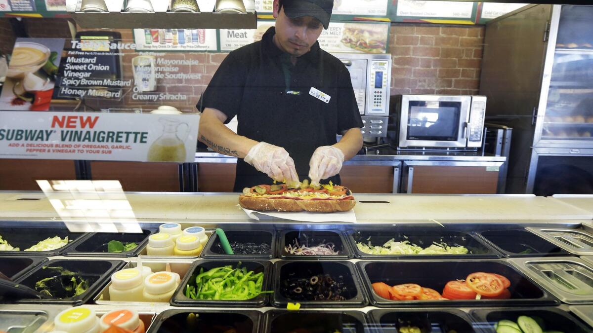 Roberto Castelan makes a sandwich at a Subway sandwich franchise in Seattle in 2015. Some Subway franchise owners say the $5 Footlong promotion loses money for them.