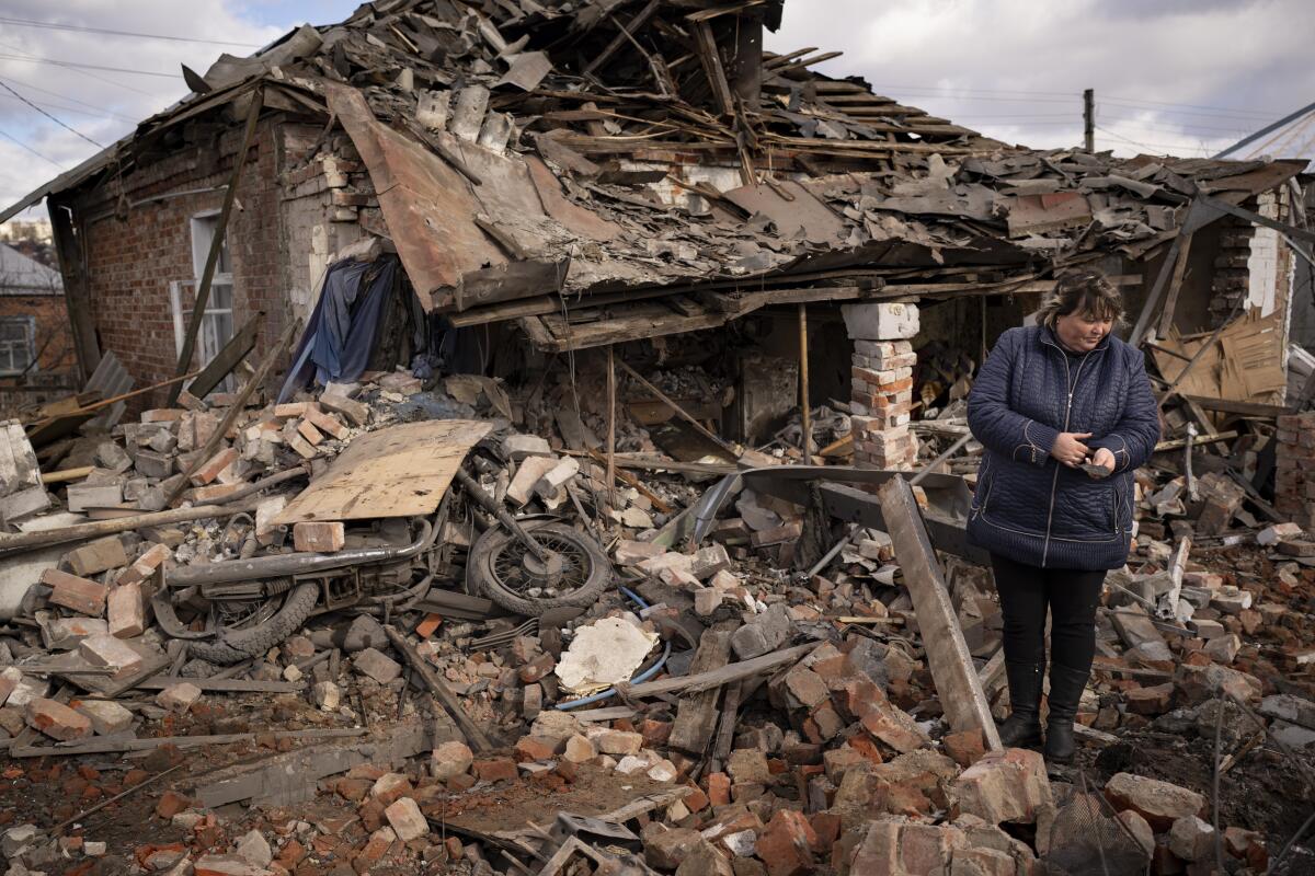 Woman holding shrapnel while standing in rubble of destroyed house