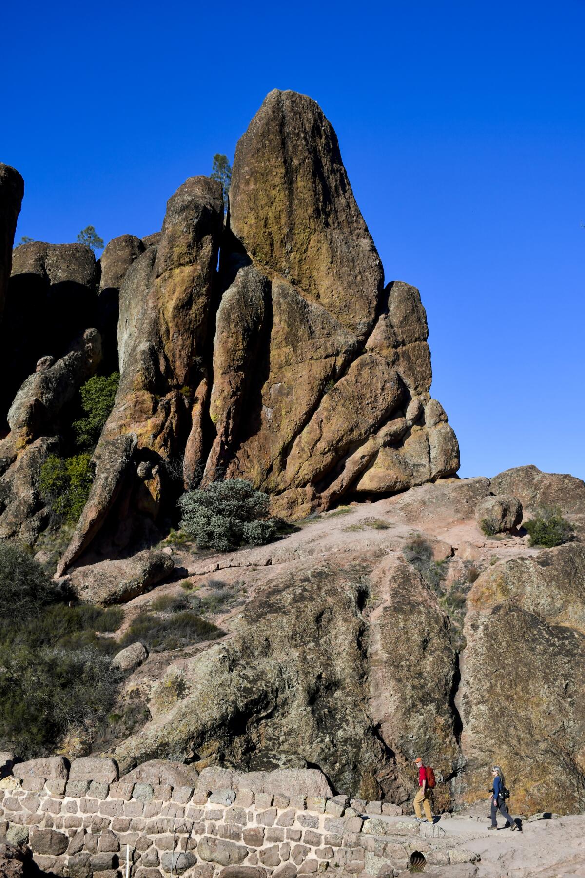 People walking a trail in front of a rocky pinnacle