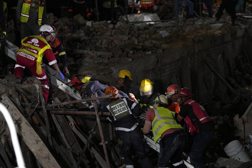 A survivor is bought to the surface at the scene of a building collapse in the city of George, about 400 kilometers (250 miles) east of Cape Town, South Africa, Tuesday, May 7, 2024. Rescue teams trying to find dozens of construction workers missing since a multi-story apartment complex collapsed in a coastal city in South Africa have made contact with 11 people buried alive beneath the mangled wreckage, authorities said Tuesday. (AP Photo/Nardus Engelbrecht)