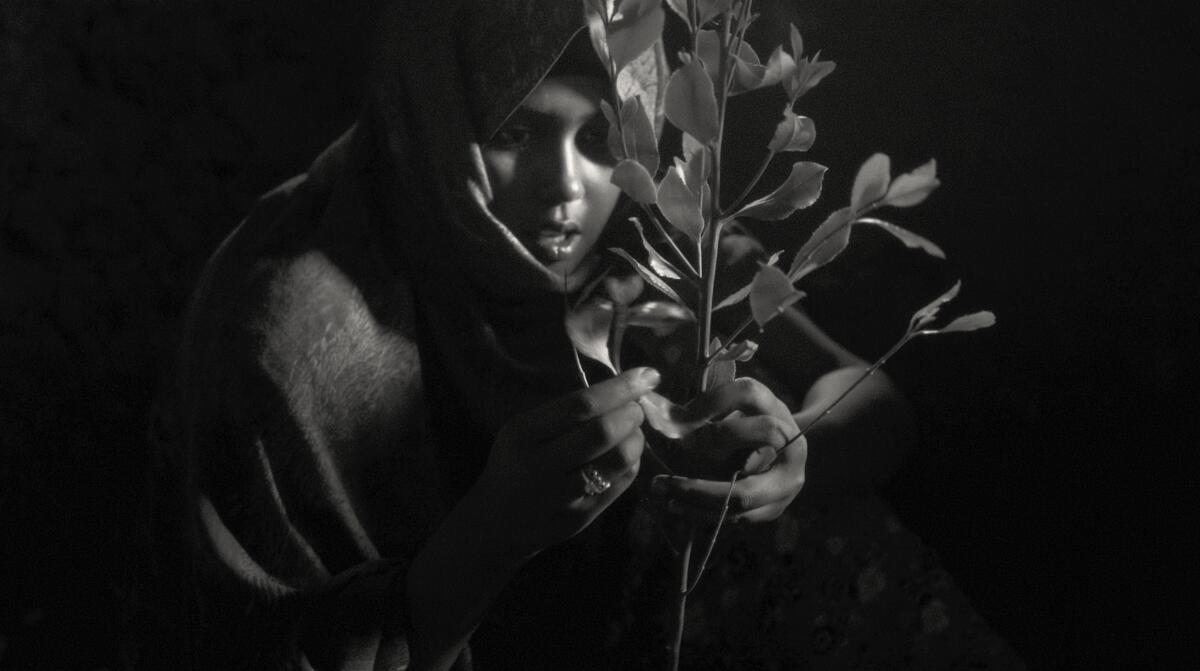 An Ethiopian from the Oromo people holds a plant in a black-and-white shot from the documentary “Faya Dayi.” 