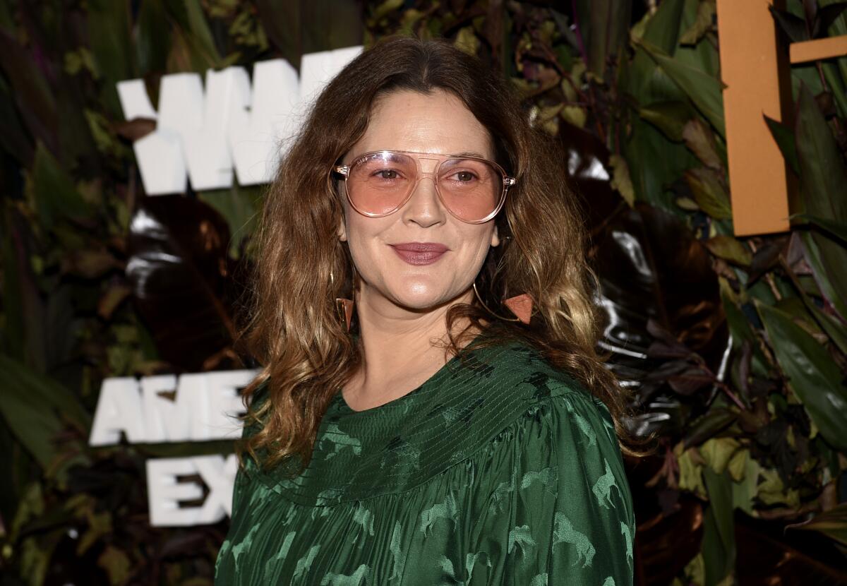 Drew Barrymore wears a green blouse and aviator shades with pink lenses and smiles over her sholder. 