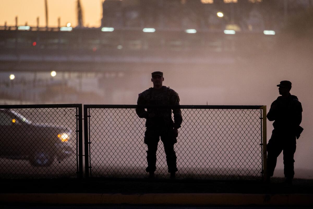 Two soldiers silhouetted against a fence and fog