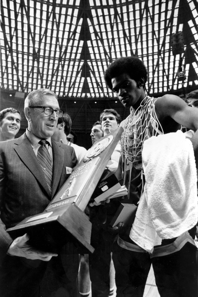 UCLA coach John Wooden holds the championship trophy and Sidney Wicks wears the net around his neck.