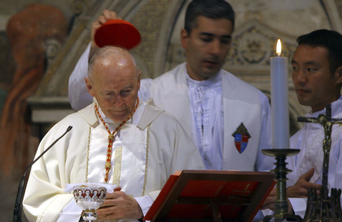 FILE - In this April 14, 2005 file photo, an aide covers the head of Washington, D.C. Cardinal Theodore McCarrick during a Mass in St. Nereus and Achilleus Church in Rome. On Tuesday, Nov. 10, 2020, the Vatican is taking the extraordinary step of publishing its two-year investigation into the disgraced ex-Cardinal McCarrick, who was defrocked in 2019 after the Vatican determined that years of rumors that he was a sexual predator were true. (AP Photo/ Alessandra Tarantino, File)