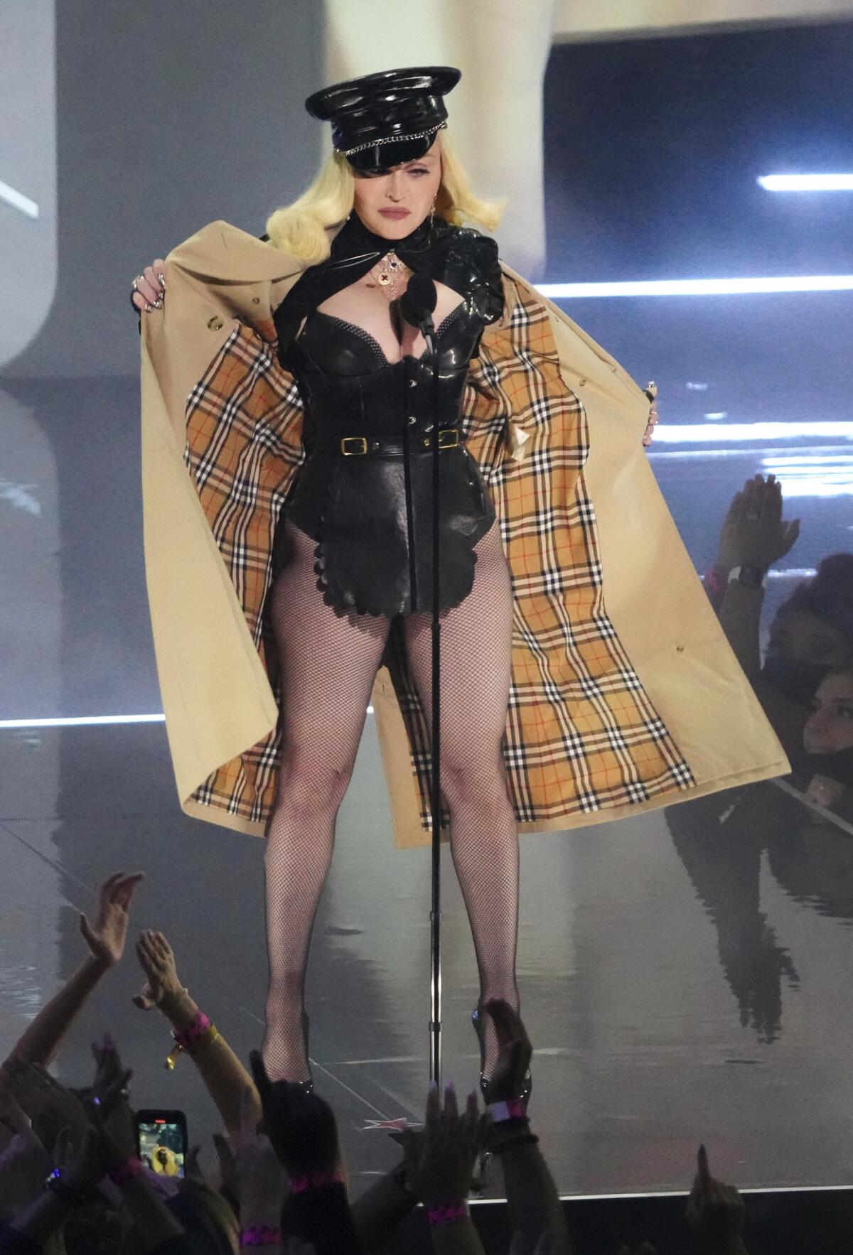 A woman stands onstage opening her trench coat to reveal a sexy outfit.