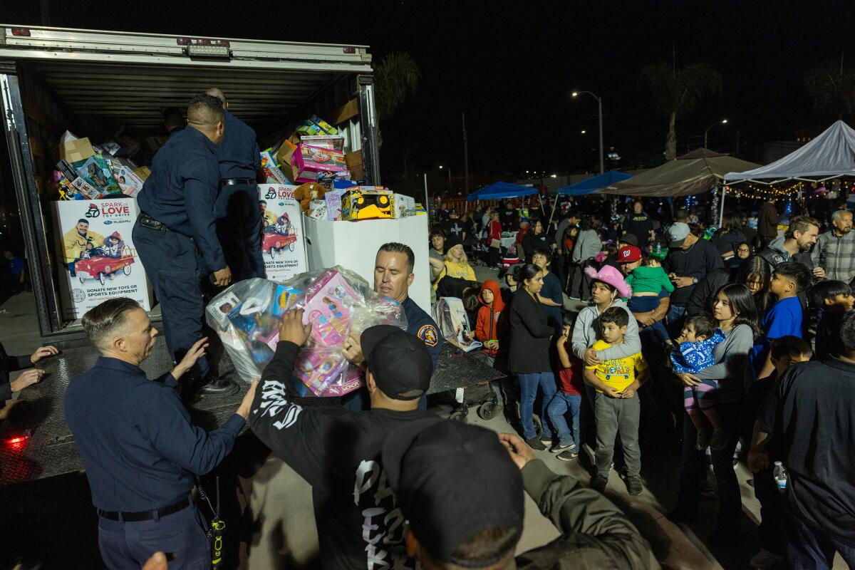 A crowd of people stand near a truck packed with wrapped gifts at night.