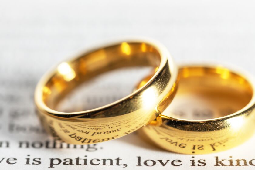 Two golden wedding rings on Bible close up above "Love is patient. Love is kind."