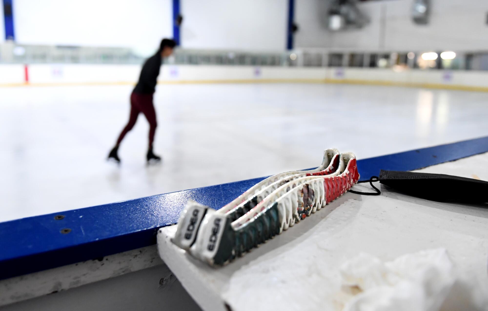 Mexican figure skater Donovan Carrillo practices as his blade guards with the Mexican flag on them sit near the ice rink.