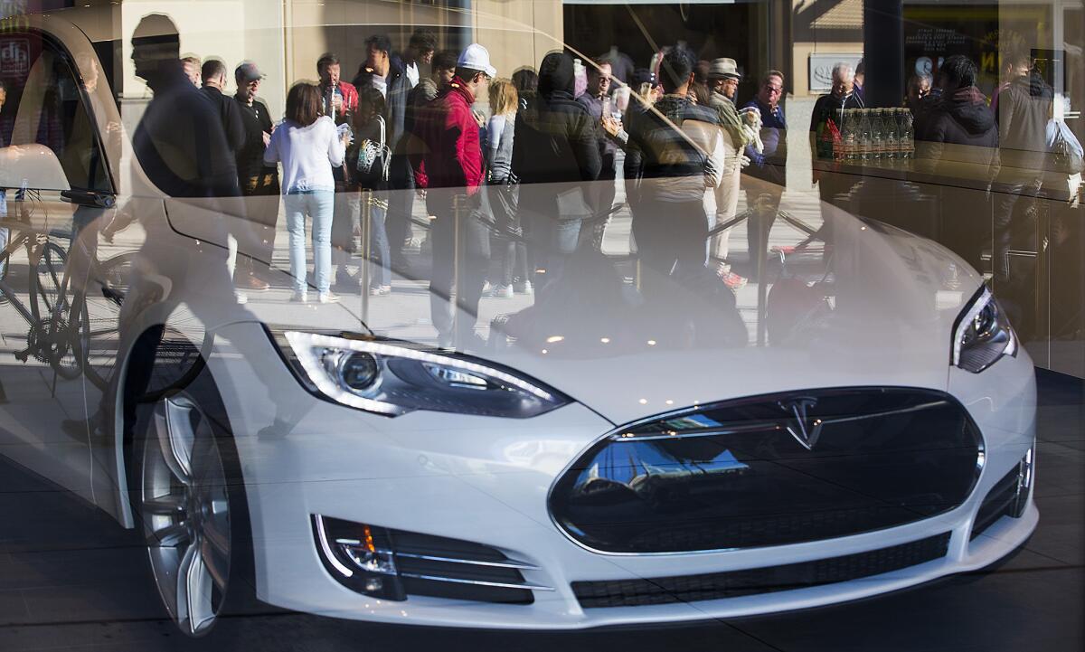 Prospective customers for Tesla's Model 3 sedan are shown in the reflection of a Model S at a Santa Monica showroom in 2016. Hundreds waited in line to put down $1,000 deposits and get on the delivery list for the new car.
