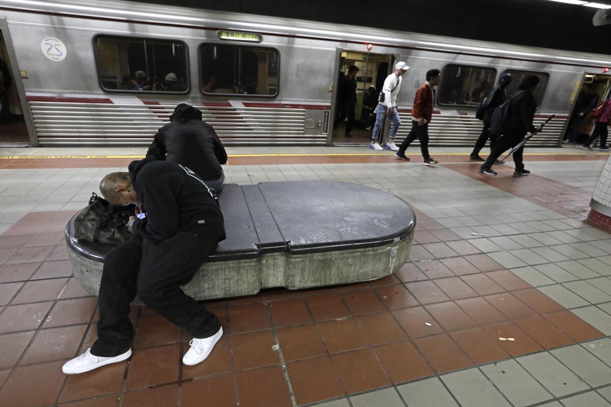 A homeless man lays on a bench in the train station.