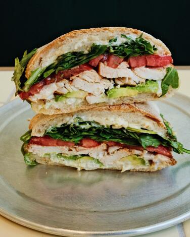 Two stacked halves of Carla Cafe's garlic-aioli chicken sandwich on a silver tray at the cafe on West 3rd Street