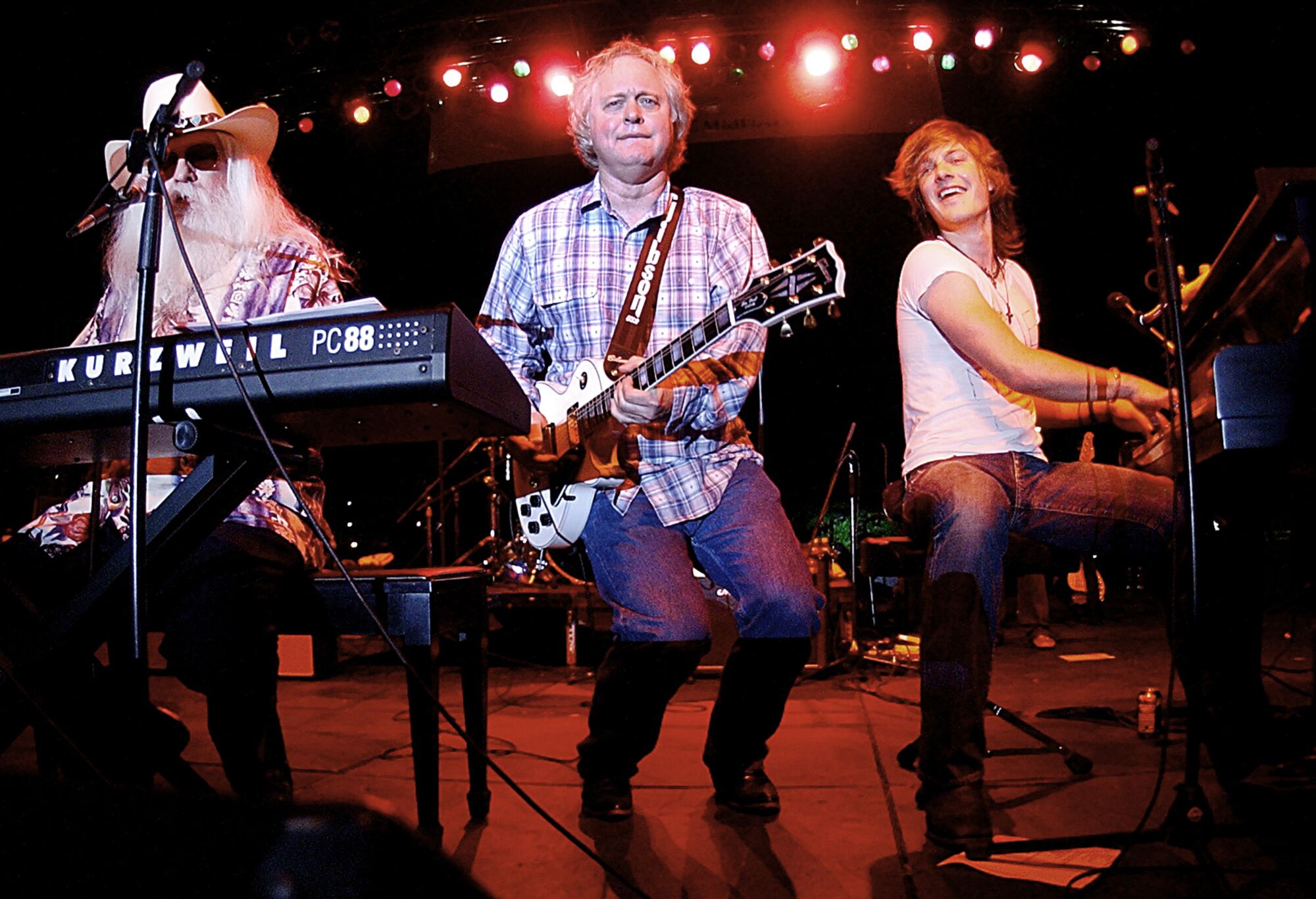 Three musicians on a stage, with Leon Russell at a keyboard.
