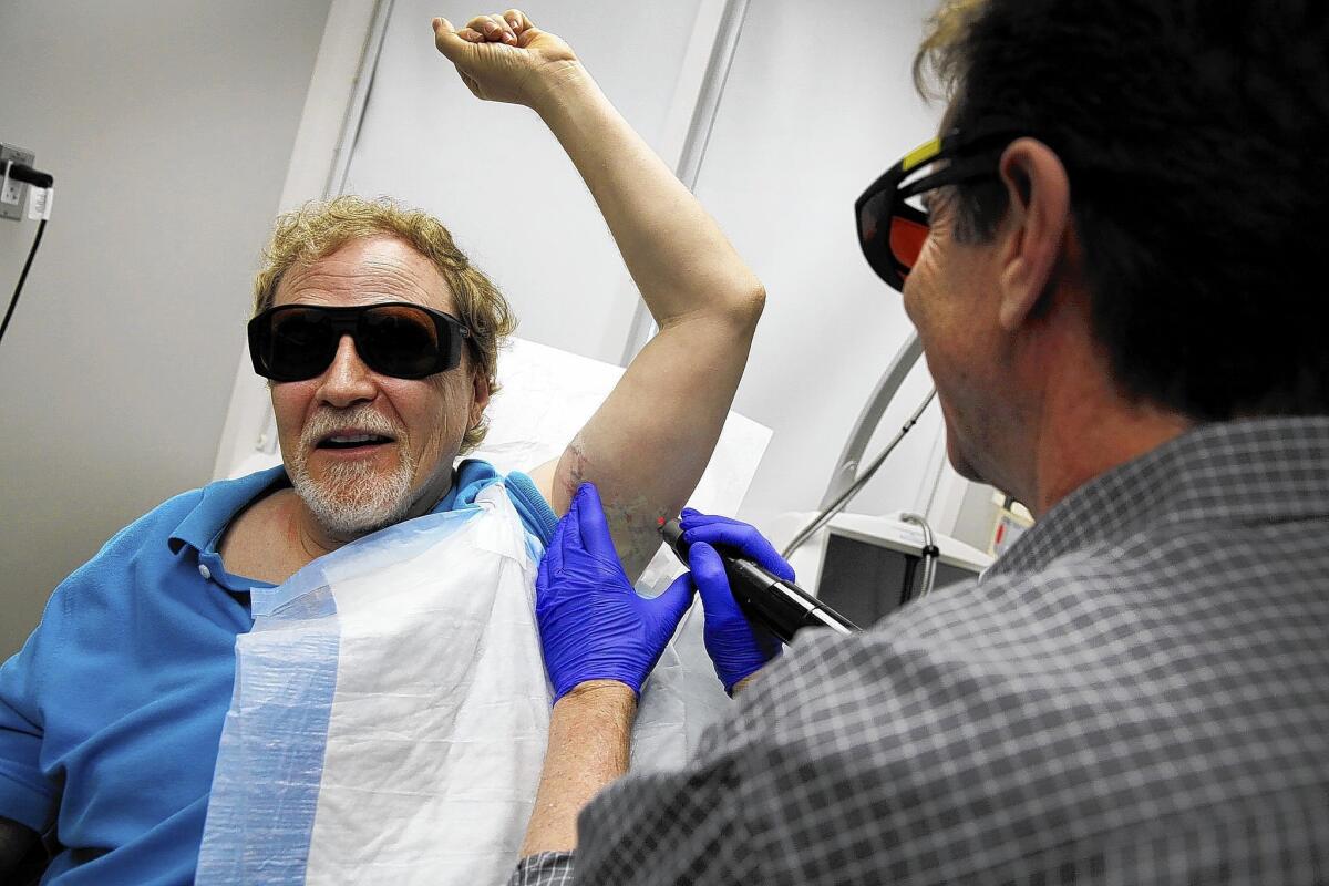 Wearing dark glass to protect their eyes, Dr. Gary Lask at UCLA uses a specialized laser to work on removing a tattoo from the arm of Stuart Yellen.