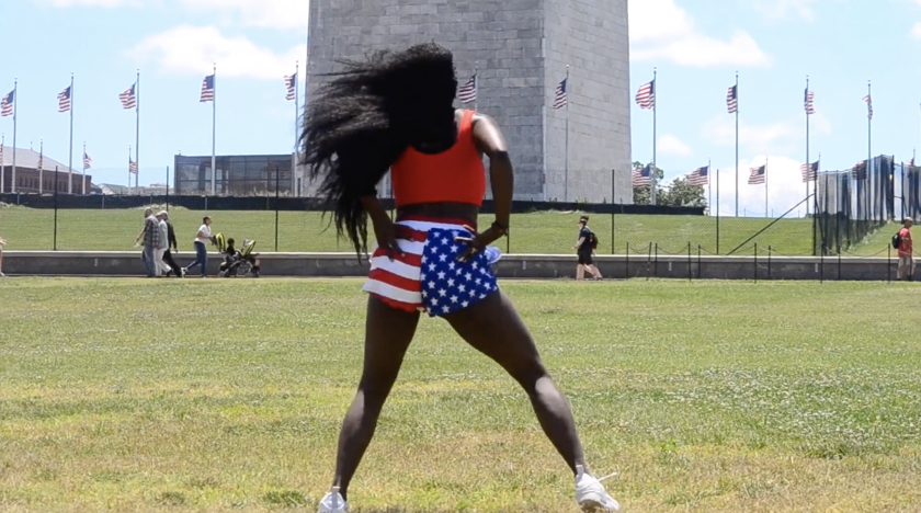 A woman in American flag shorts stands with her back to the camera in the grassy National Mall.