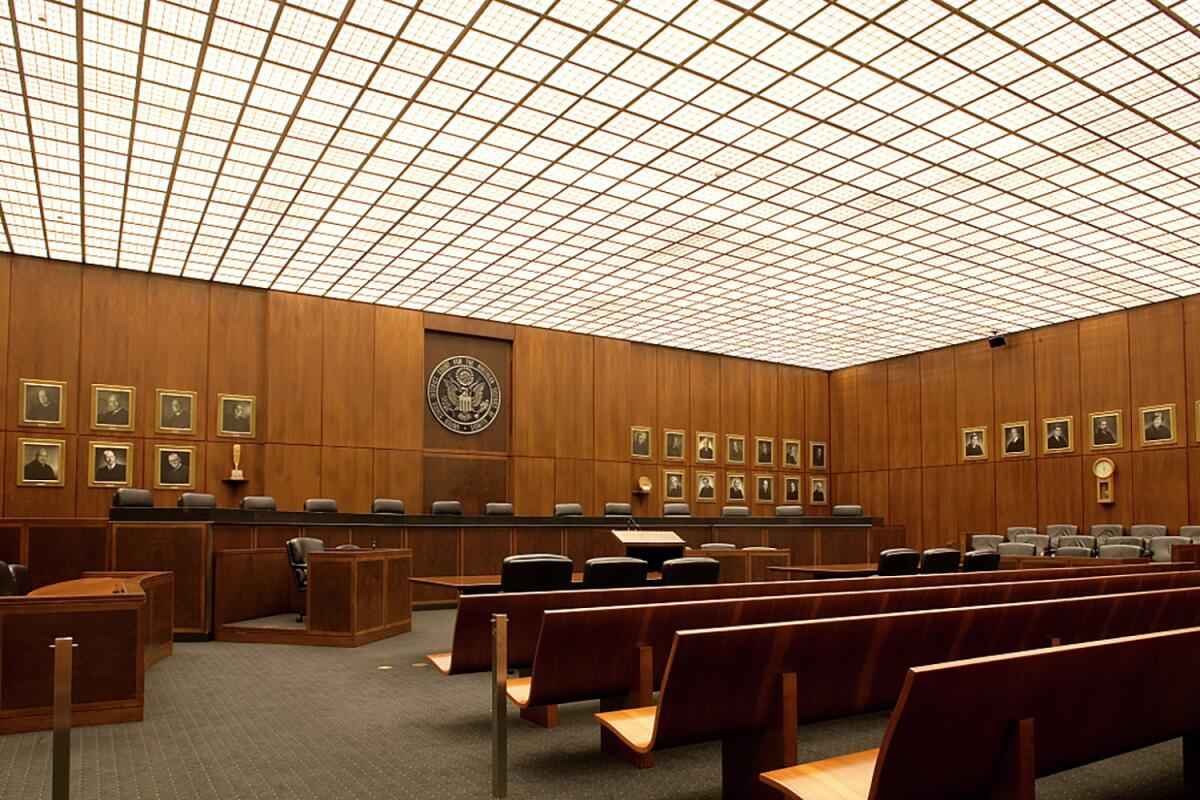 A courtroom with portraits on brown-paneled walls and empty benches 