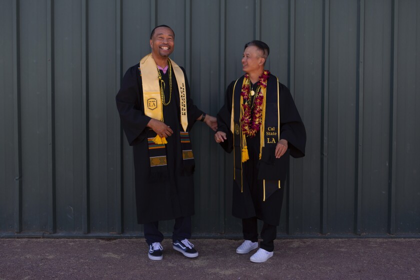 Two men smile while wearing graduation robes and sashes