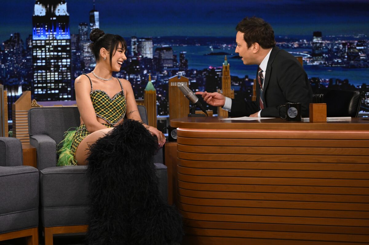 A singer being interviewed by a man seated behind a desk.