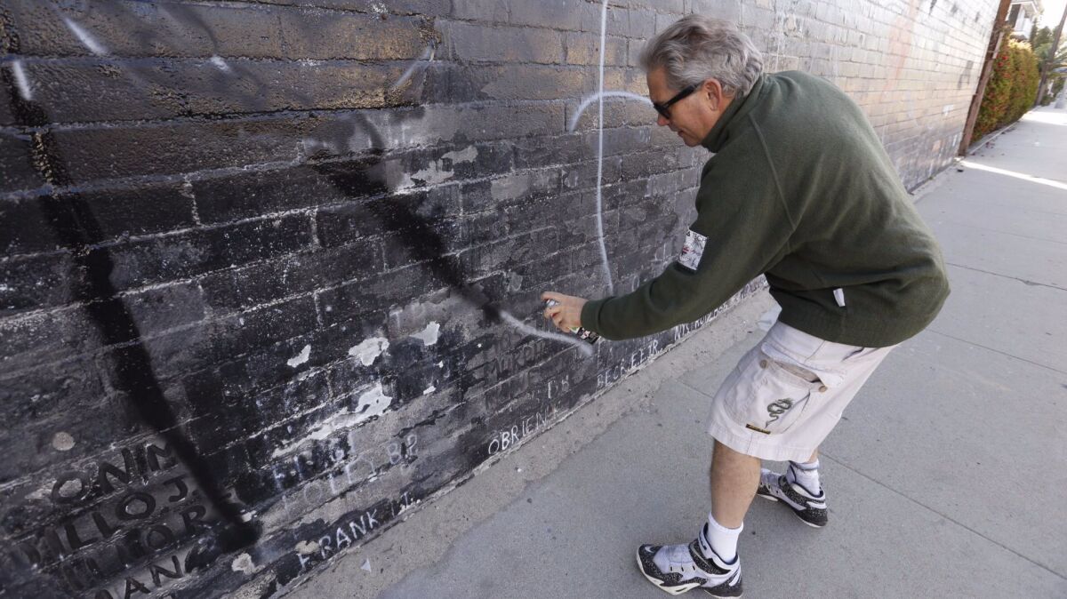 Steven Barber uses black spray paint to cover the white letters of graffiti on the wall. (Al Seib / Los Angeles Times)