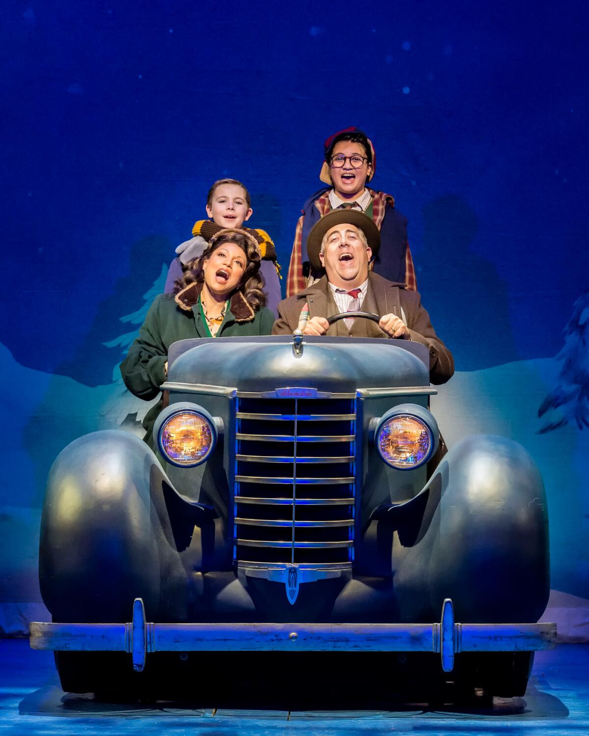 Four people sing in a vintage car onstage.