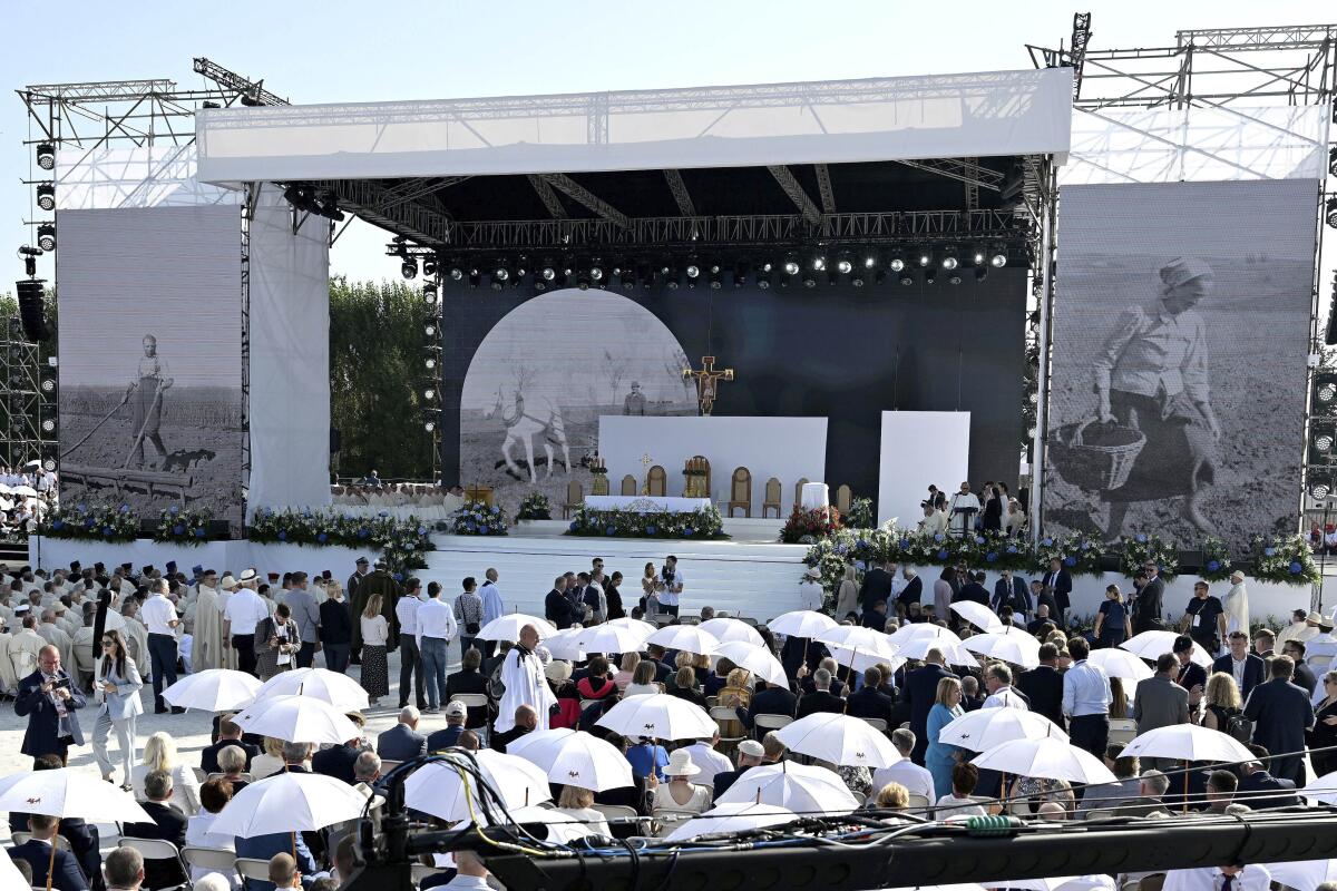 Crowd with whie umbrellas attends an outdoor Mass on a stage in which the Vatican beatified the Polish Ulma family.