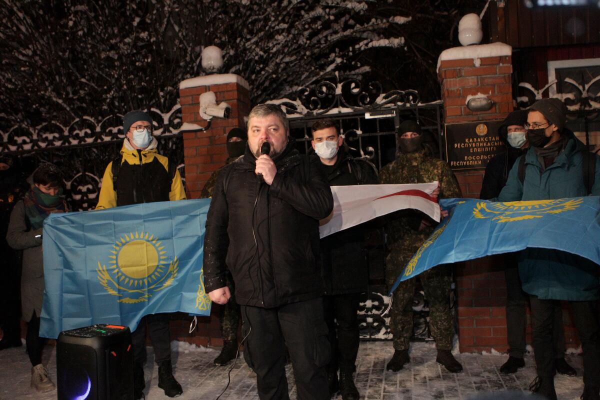 Ukrainian activist Maksym Butkevych speaking at a rally in Kyiv flanked by demonstrators holding flags.