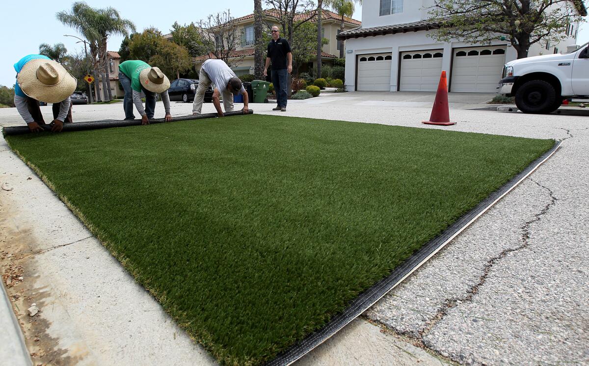 Workers roll up a pre-measured piece of artificial grass for installation in the backyard of a home in Pacific Palisades.