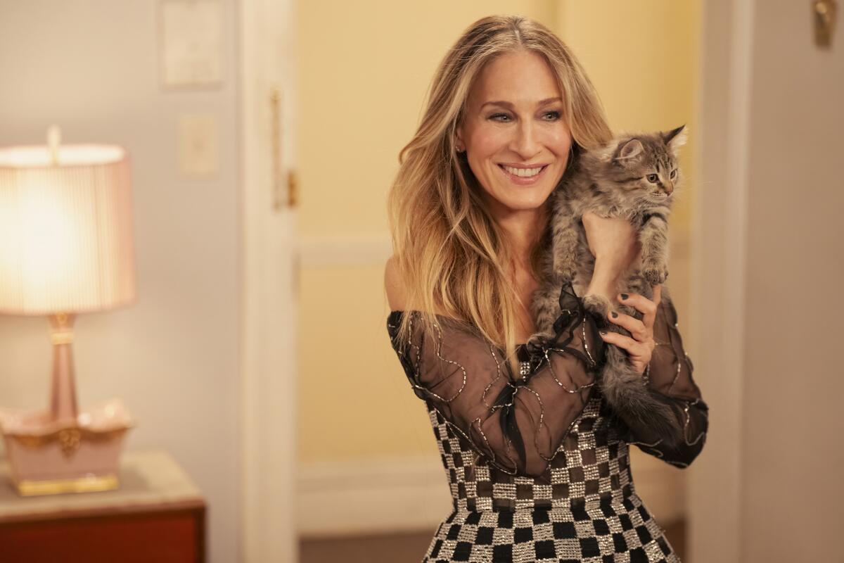 Sarah Jessica Parker stands in a room with a lamp and holds a cat near her face