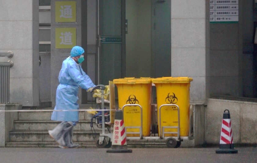 A staff member wears protective gear to move biological waste containers outside the Wuhan Medical Treatment Center, 