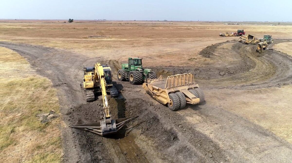 Earth-moving equipment scrapes tracks in bare land