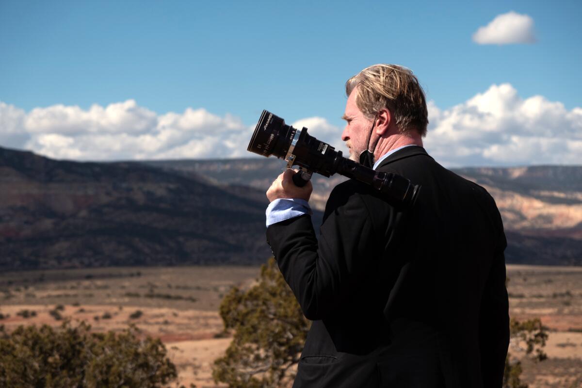 A man looks through a camera lens in the desert.