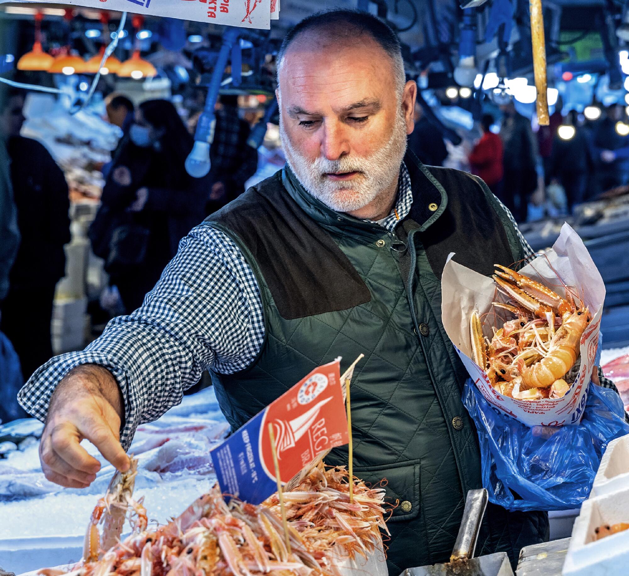 Chef José Andrés visits Athens Market in Greece. He holds a bundle of seafood under one arm at a food stall.