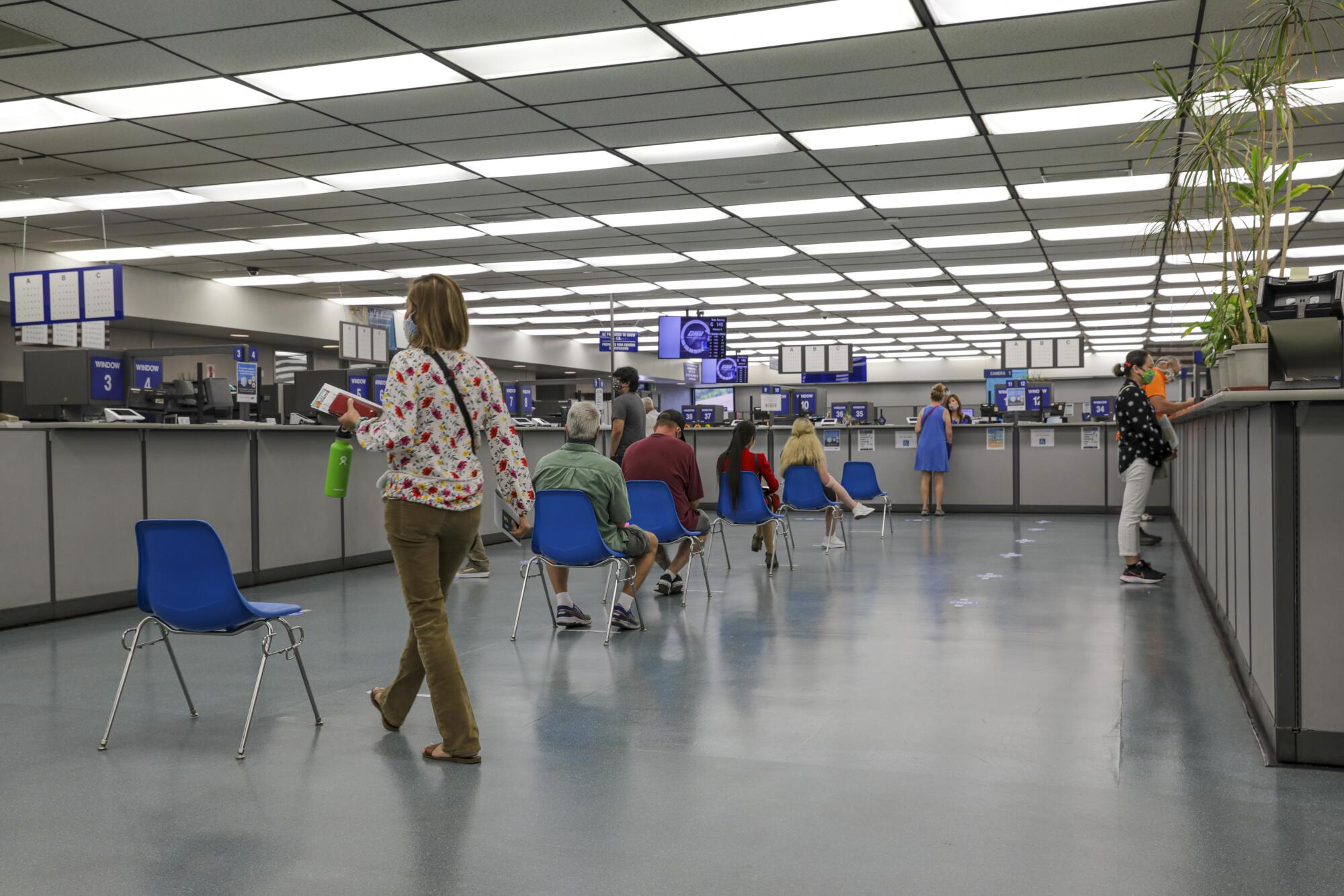Customers sit in blue chairs spaced six feet apart in a line inside a DMV field office