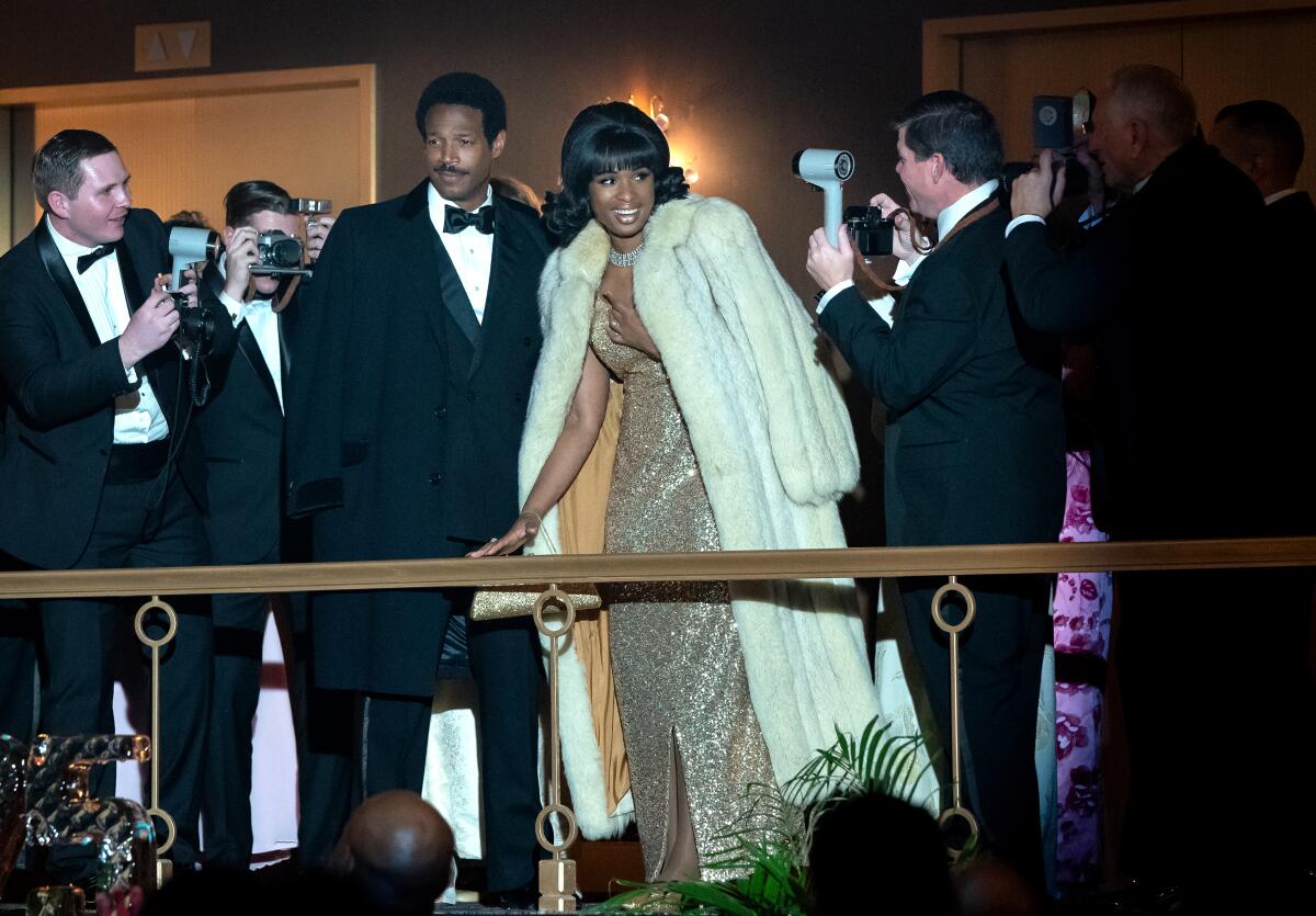 A man and woman in eveningwear are surrounded by photographers.