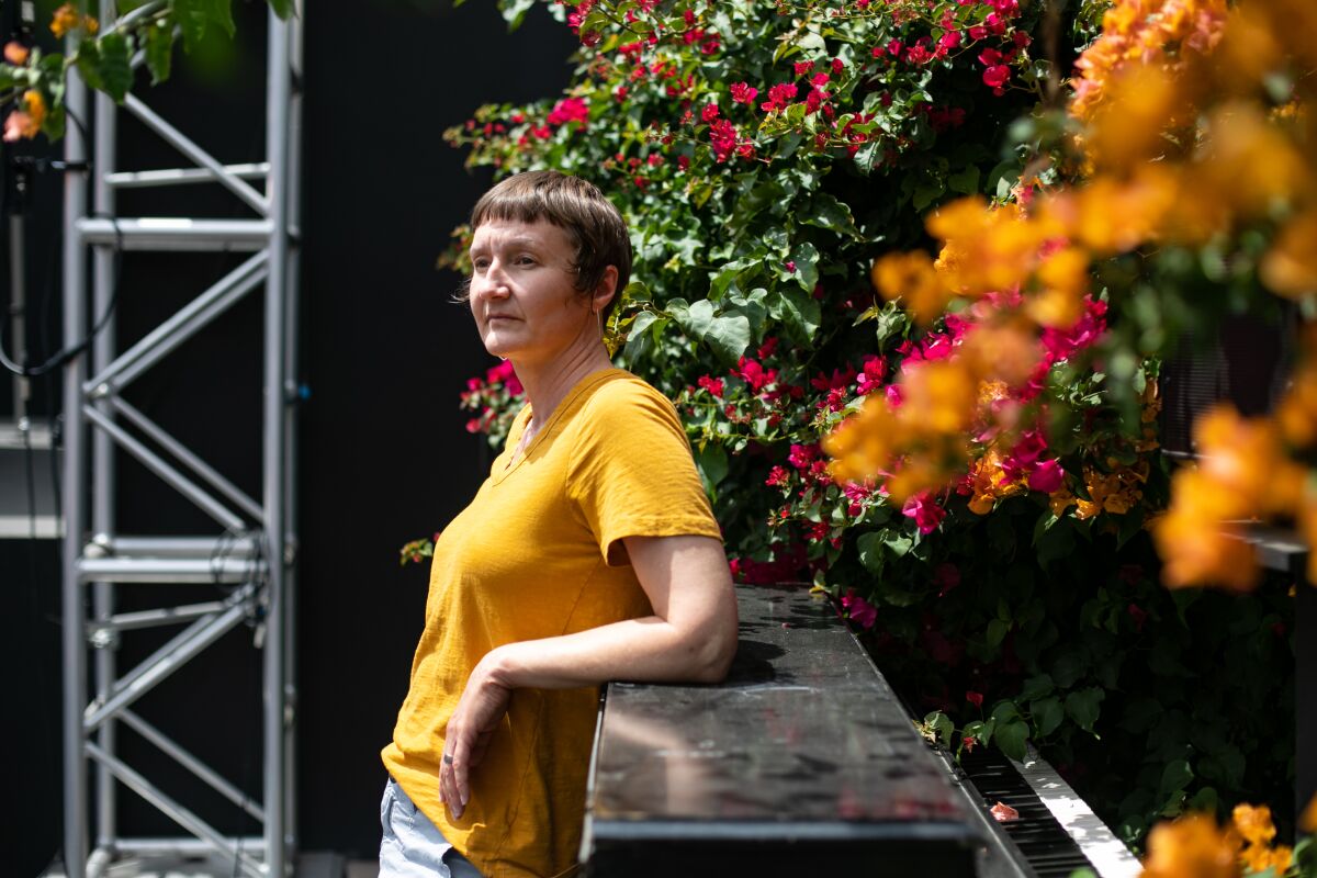 A person in a yellow T-shirt stands outside amid flowering shrubs.