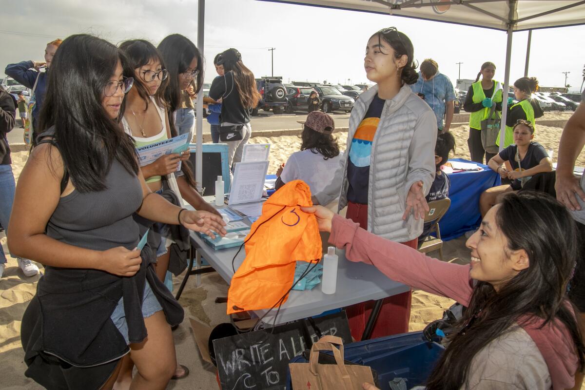 Vanguard University student Beverly Alvarez, center, welcomes volunteers to the coastal cleanup at Huntington State Beach.