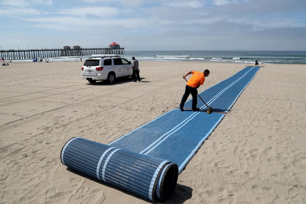 A worker sweeps sand off the first Mobi-Mat in Huntington Beach before a ribbon-cutting ceremony in 2021.