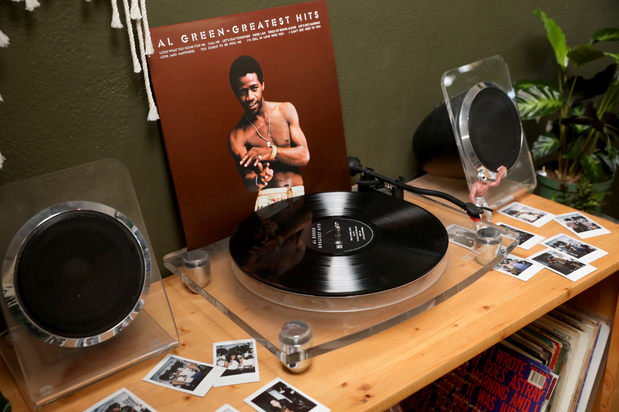 A turntable sits on a handmade case displaying an Al Green album cover, flanked by plants and Polaroid photos.