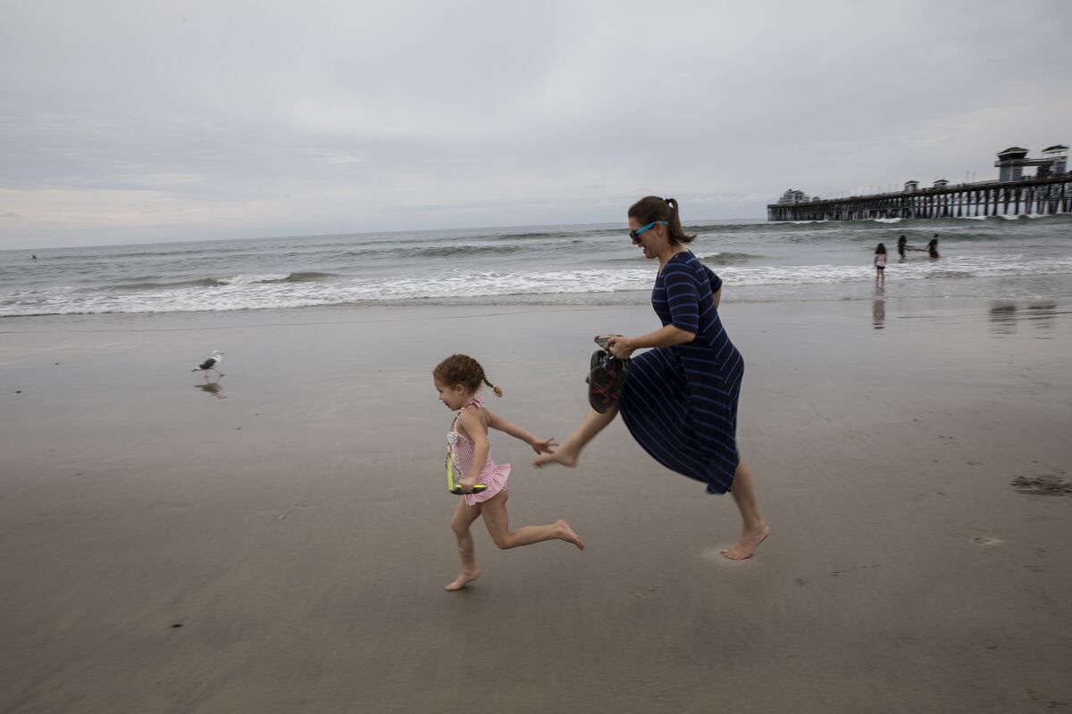 Julie Robinson runs with her daughter Adalee along the beach near the Oceanside Pier 