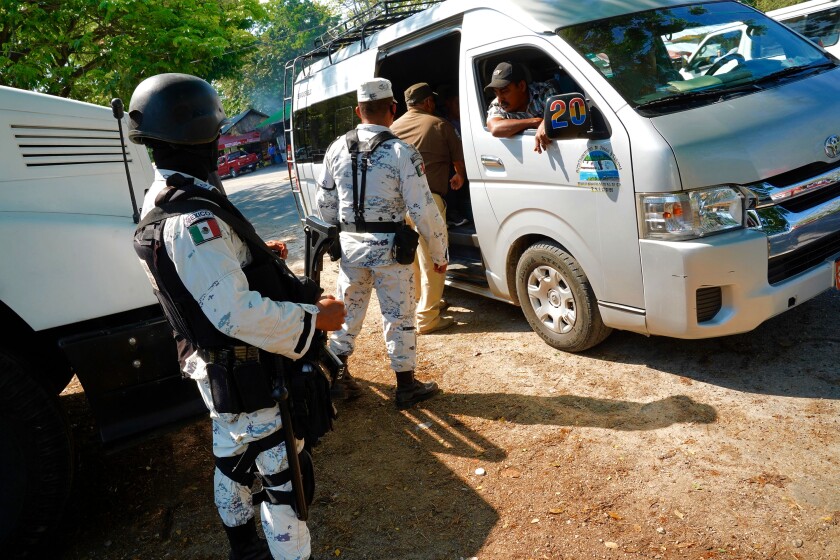 Mexican immigration agents and National Guard troops at checkpoint for vehicles.